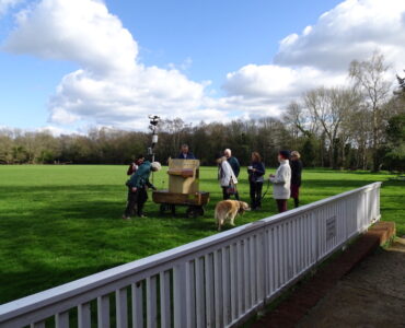 Future Machine and people gathered around on the cricket ground, with blue sky and fluffy clouds above