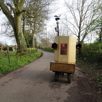 Future Machine on a country lane with a tree, gravestones and daffodils in the background