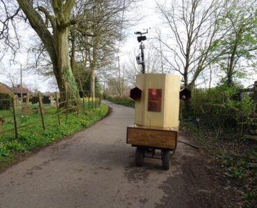 Future Machine on a country lane with a tree, gravestones and daffodils in the background