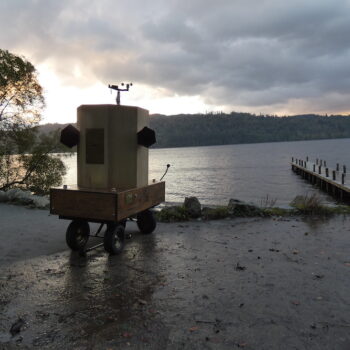 Future Machine with the lake, a jetty and the sunset behind it