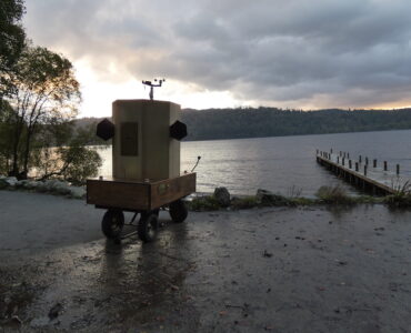 Future Machine with the lake, a jetty and the sunset behind it