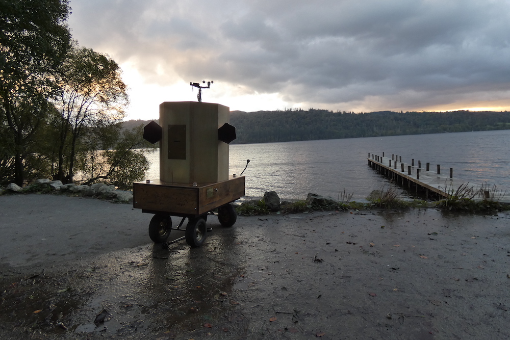 Future Machine with the lake, a jetty and the sunset behind it