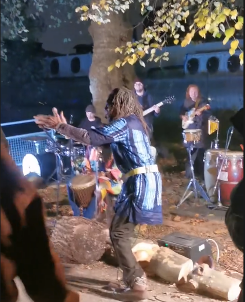 Alex clapping in front of a drummer and guitarists under a tree.