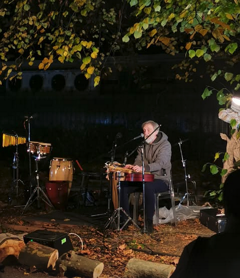 A man sitting playing a guitar under a tree.