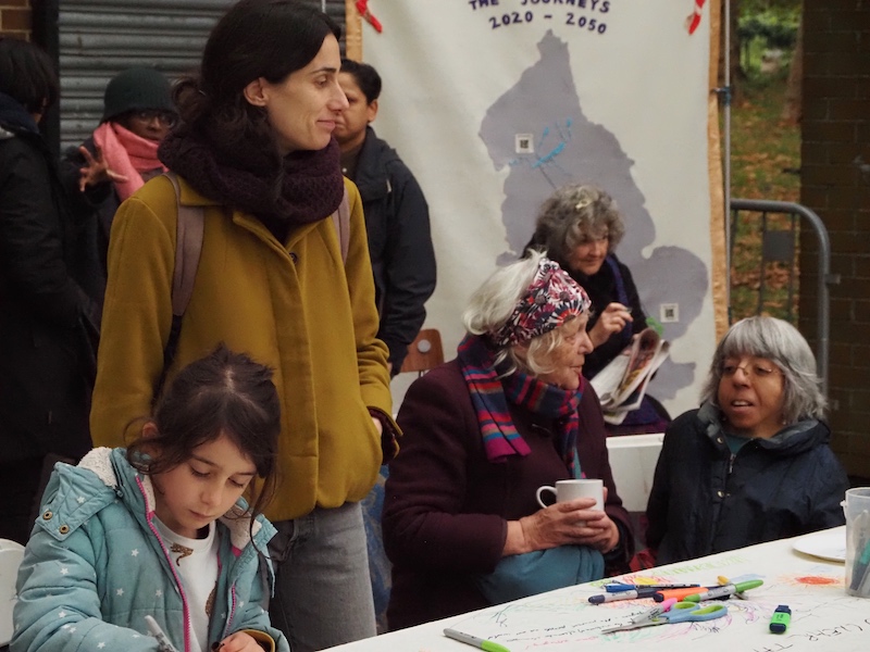 A girl drawing, a woman drinking tea. The Future Machine banner in the background.