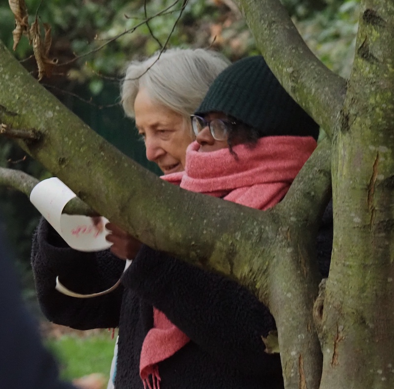 Esi attaching paper to a tree with a woman reading behind her.