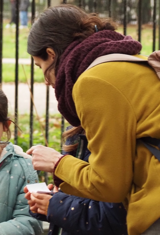 A woman pointing to a small card, held by a child.