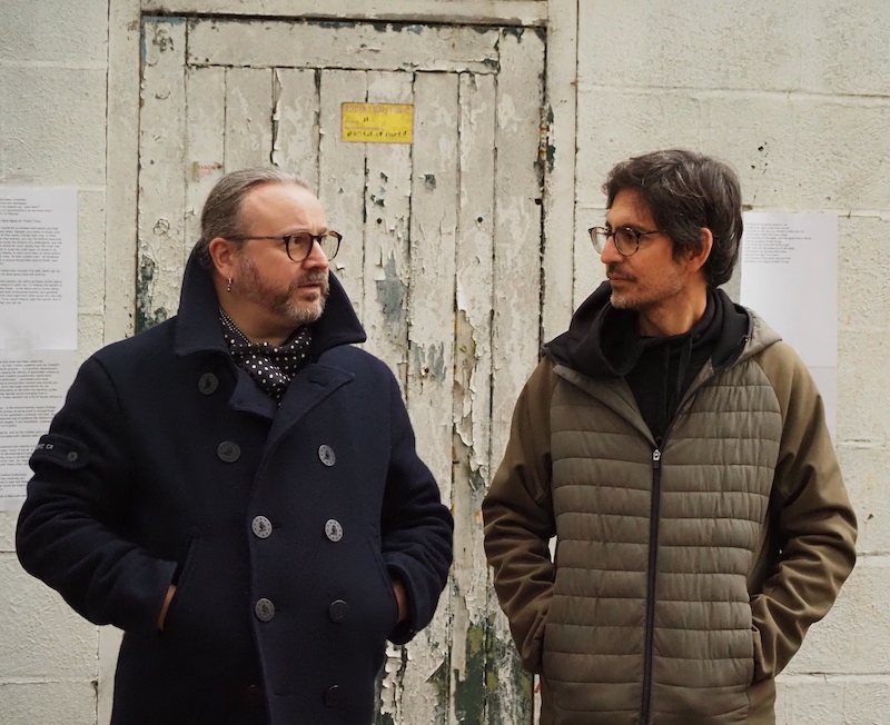 Two men talking in front of a derelict building.